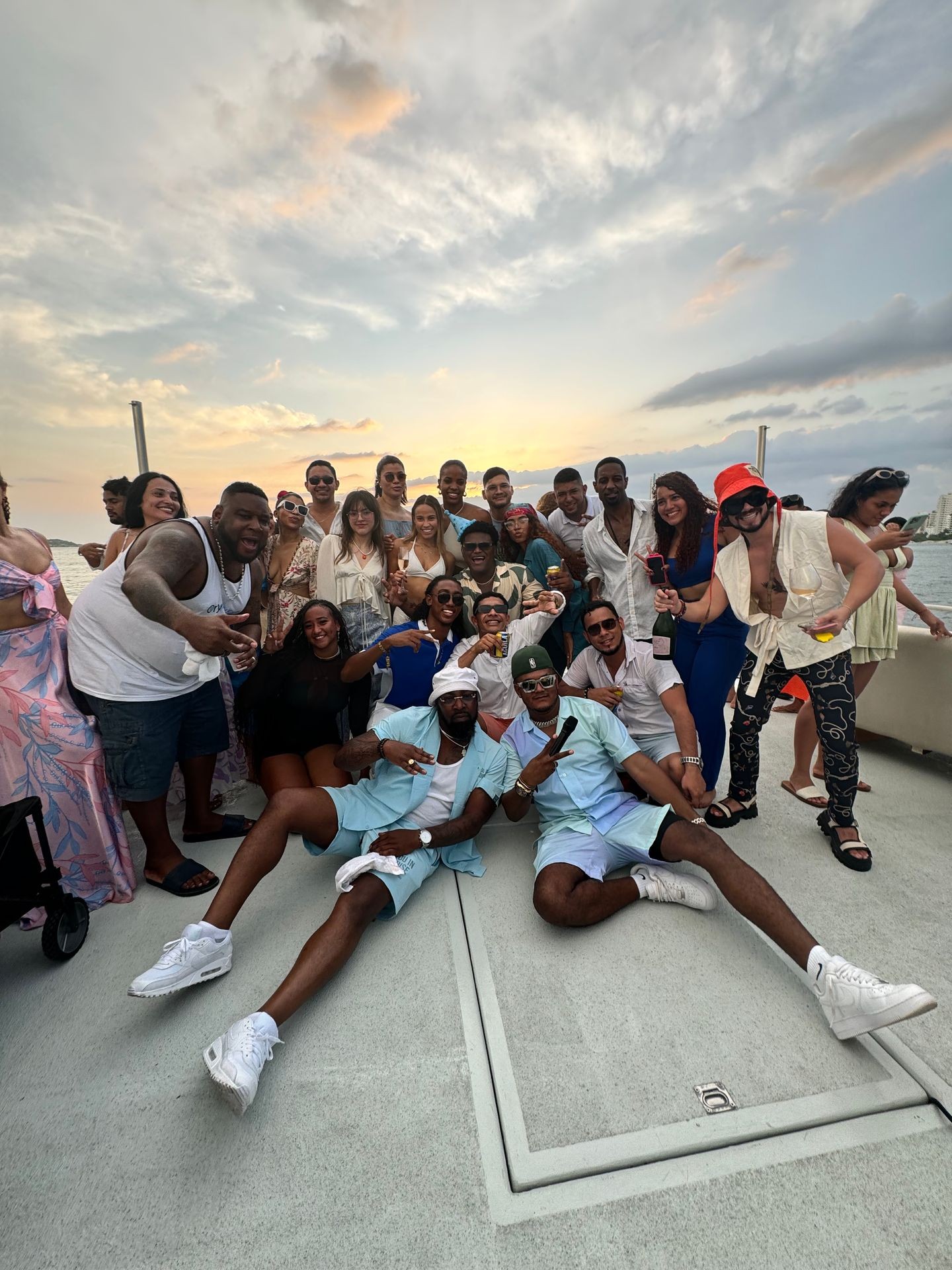 Group of people posing on a boat deck at sunset, dressed in casual summer outfits.